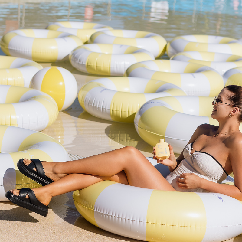 Woman lounging on a yellow and white striped pool float by a poolside.